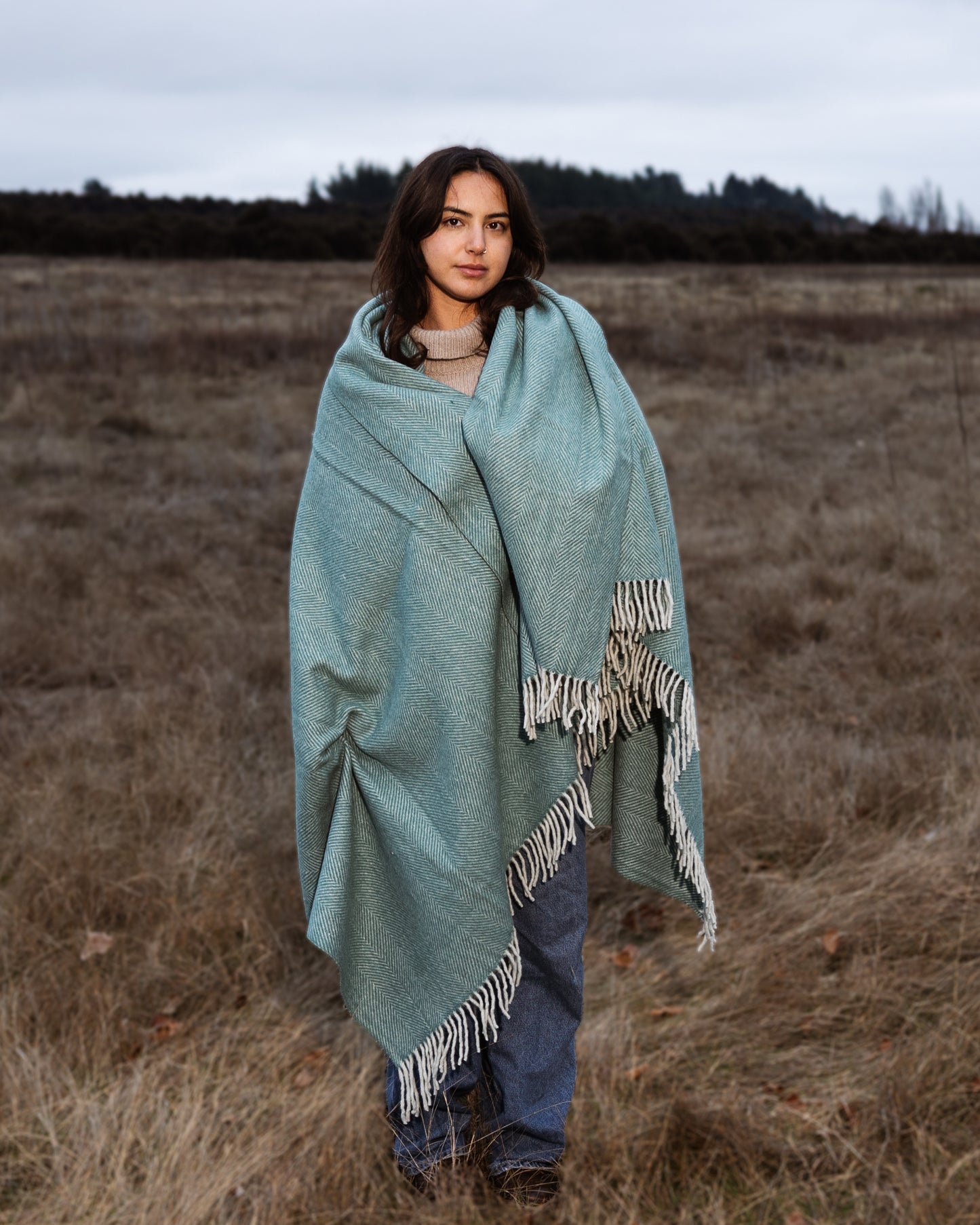 Woman wrapped in a light blue blanket standing in a field