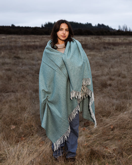 Woman wrapped in a light blue blanket standing in a field
