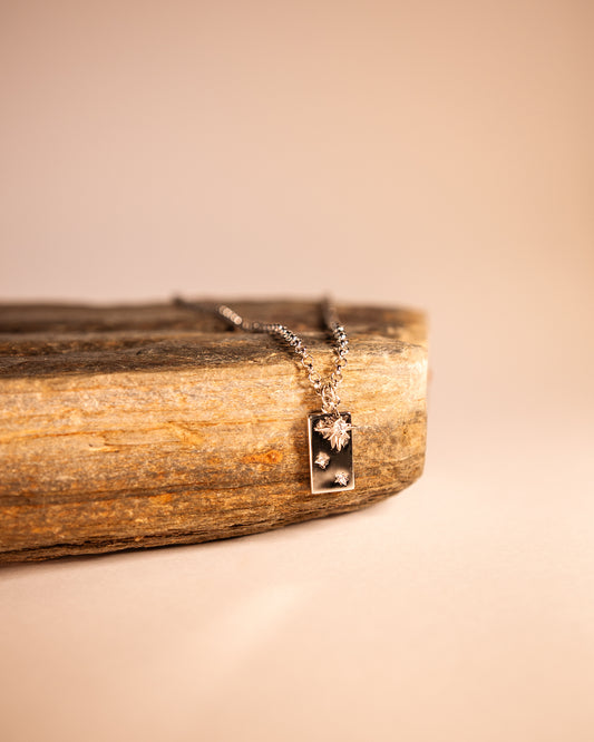 A silver necklace with a Southern Cross pendant and a separate star pendant, displayed on a wooden surface.