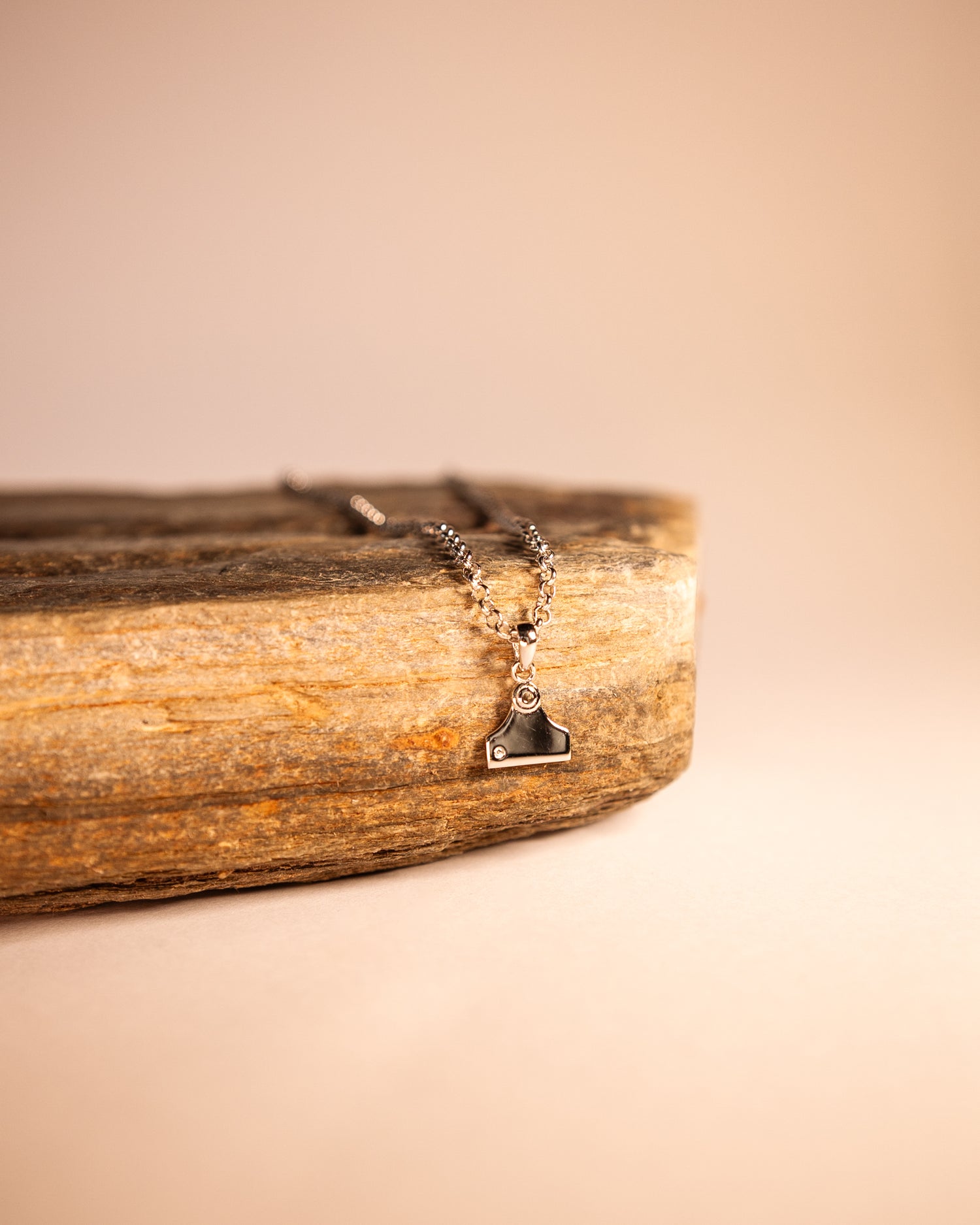 A cattle tag necklace with a white zircon stone pendant, made of sterling silver, displayed on a wooden piece.