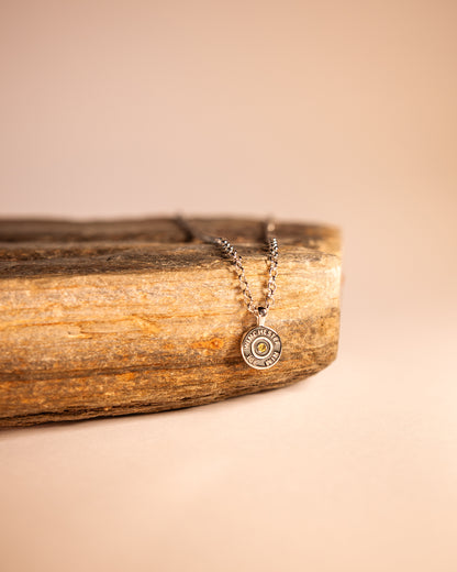 A necklace with a round olive green pendant on a 925 sterling silver chain, displayed on a wooden surface.