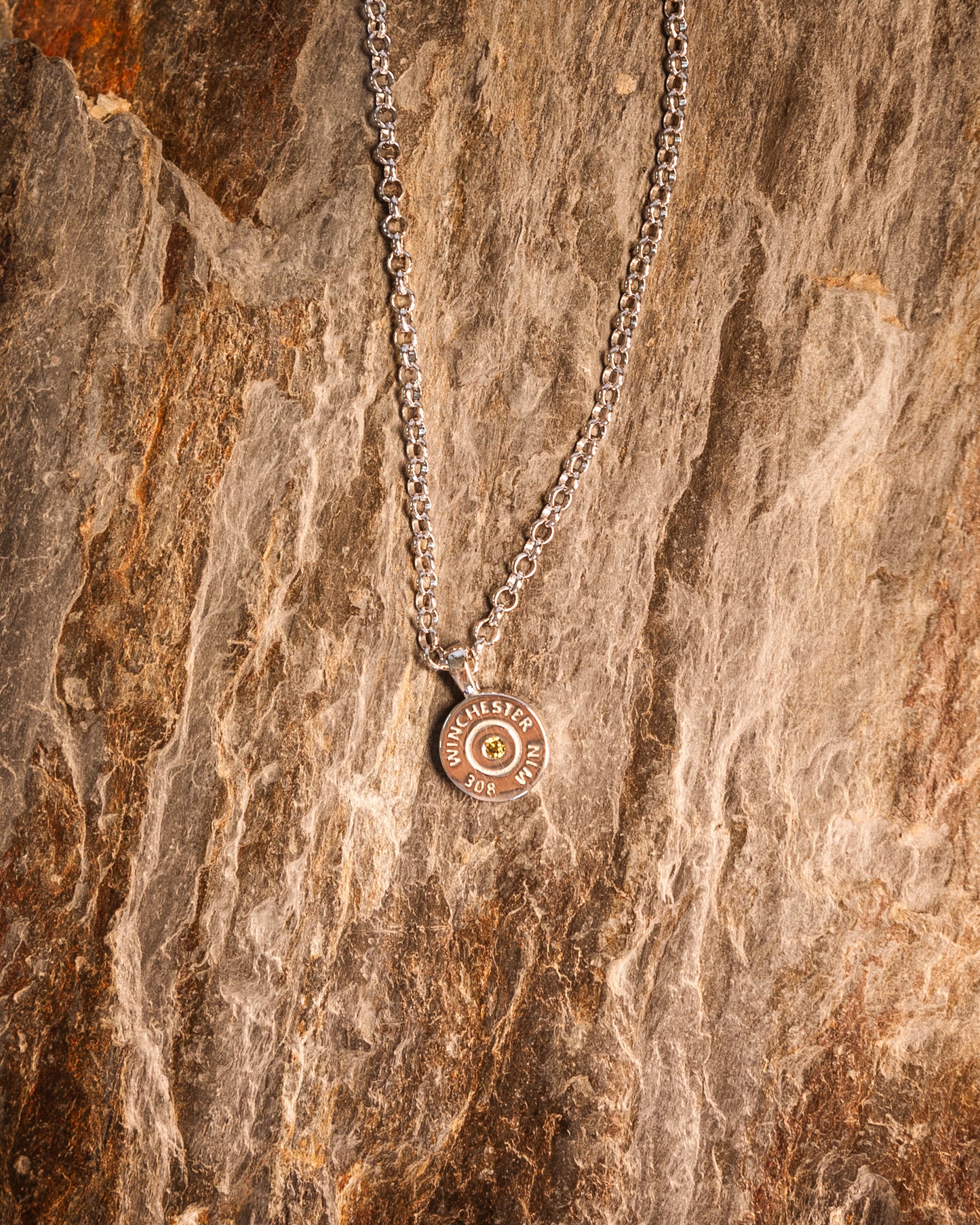 A necklace with a round olive green pendant on a 925 sterling silver chain, displayed on a wooden surface.