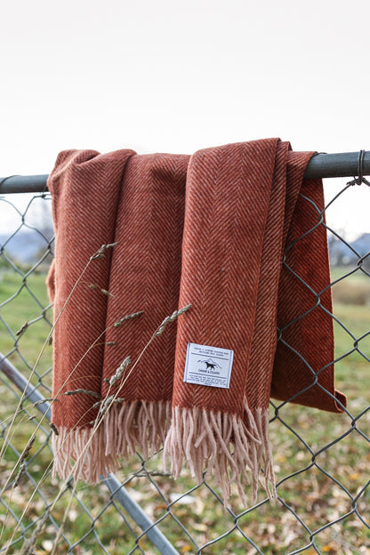 Recycled wool blanket with fringes draped over a metal fence in an outdoor setting.