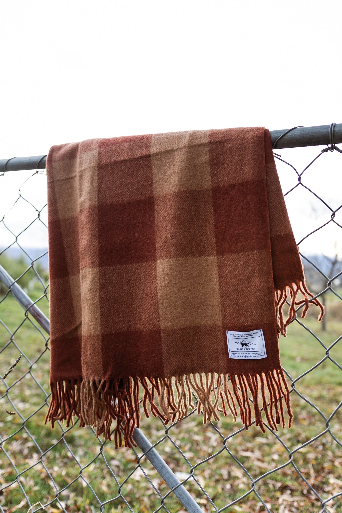 Recycled wool blanket hanging on a chain-link fence.